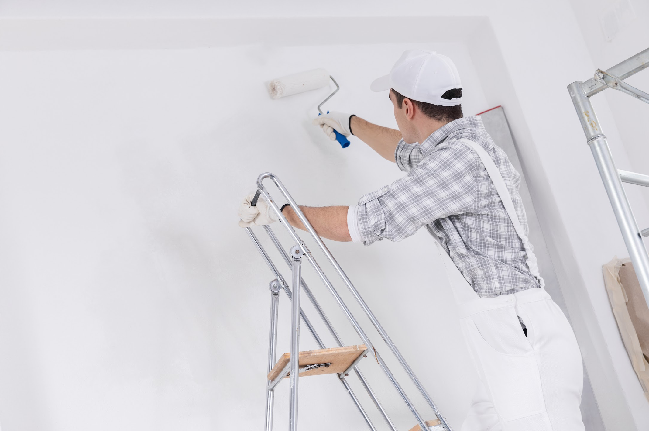 professional decorator painting wall atop ladders