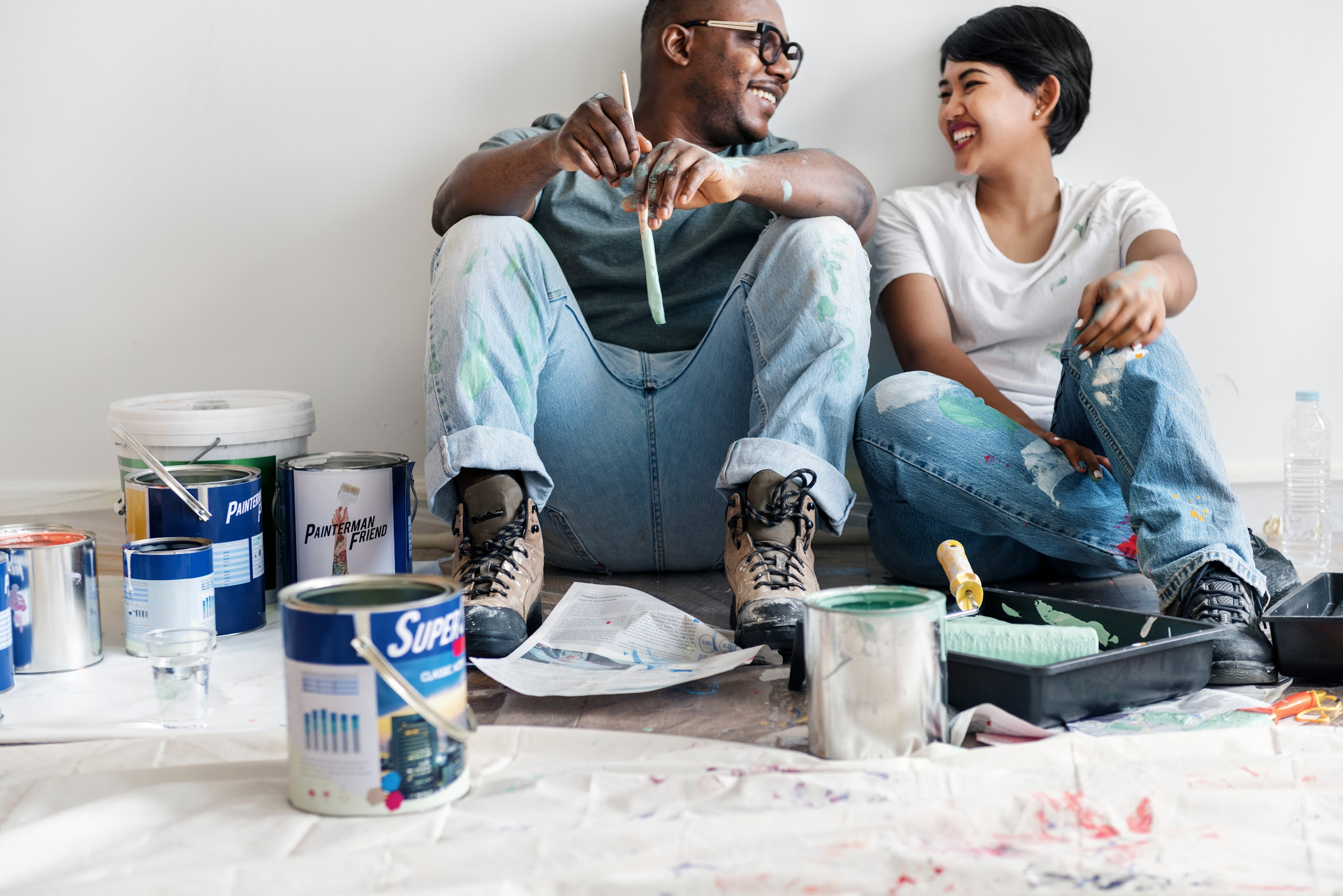 couple sat on floor surrounded by paint pots laughing